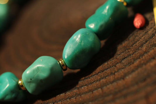 Turquoise bracelet with south red agate displayed on a wooden background, highlighting the unique turquoise stones and gold accents.